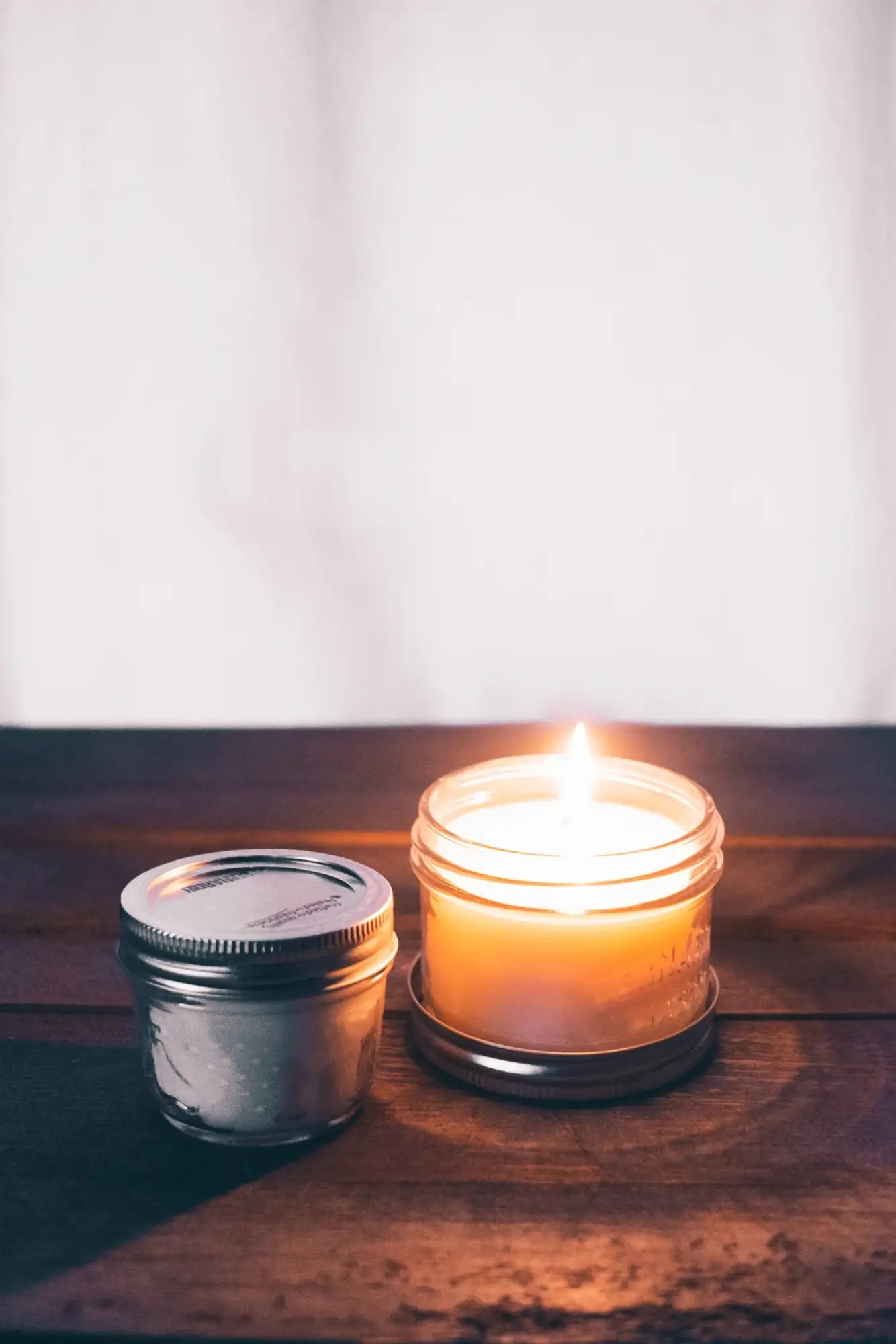 A lit orange candle in a clear glass jar with a metal lid.